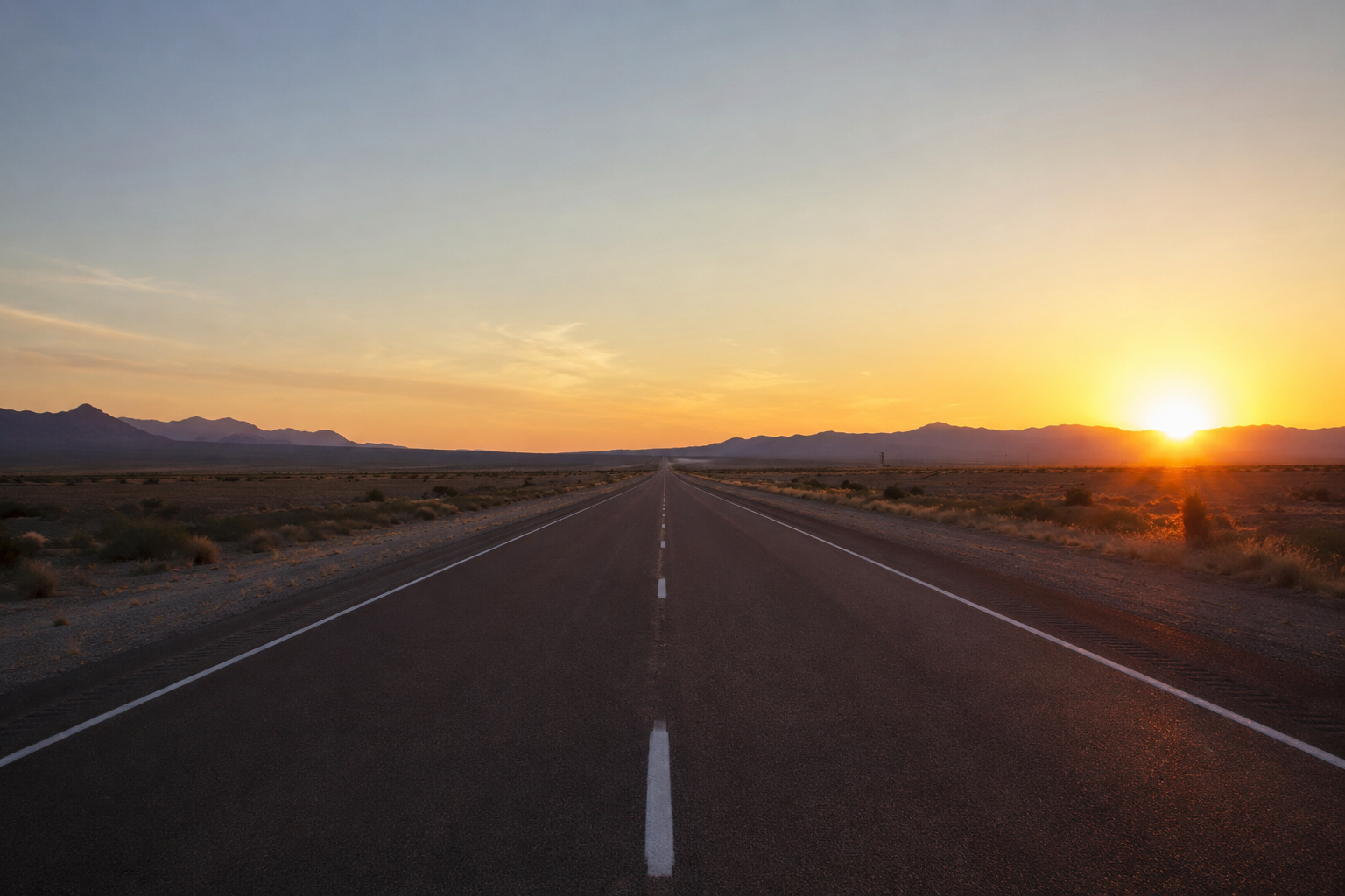 Open desert highway leading toward a bright sunrise